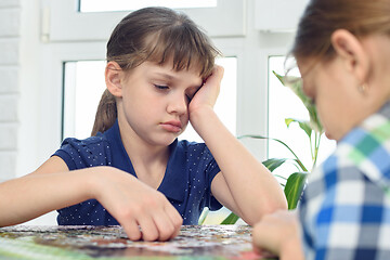 Image showing Tired girl reluctantly collects jigsaw puzzles with her friend