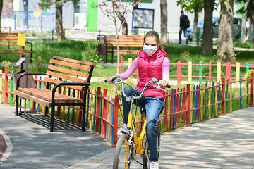 Image showing Girl rides a bicycle near the playground in a medical mask