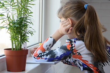 Image showing A teenager looking away from the camera draws with a pencil in an album sitting on the floor in front of the window