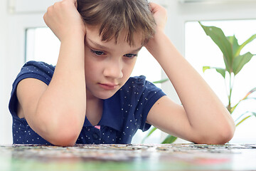 Image showing Girl thinking over a puzzle while sitting at home at the table