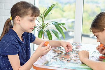 Image showing Two girls collect puzzles at the table and eat carrots