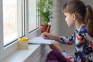 Image showing Girl draws with a pencil in an album on the windowsill
