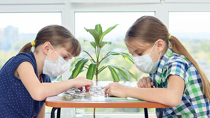 Image showing Two girls in medical masks sit at a table and play board games.