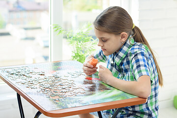 Image showing Girl at home by the window collects puzzles on his day off