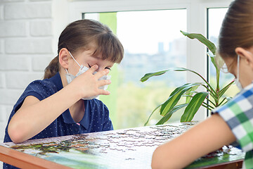 Image showing A sick masked girl scratches her eyes with dirty fingers