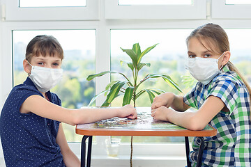 Image showing Two girlfriends in medical masks play puzzles and looked into the frame.