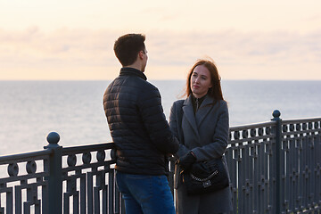 Image showing Girl anxiously looks at a guy near a railing in the background of the sea in cloudy weather