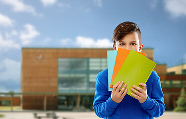 Image showing shy student boy hiding behind books over school