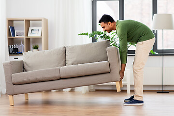 Image showing happy indian man moving sofa at home