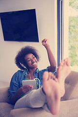 Image showing African american woman at home in chair with tablet and head pho