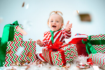 Image showing Cute baby girl 1 year old near santa hat posing over Christmas background. Sitting on floor with Christmas ball. Holiday season.