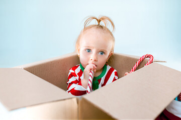 Image showing Cute baby girl 1 year old sitting at box over Christmas background. Holiday season.