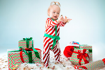 Image showing Cute baby girl 1 year old wearing santa hat posing over Christmas background. Sitting on floor with Christmas ball. Holiday season.