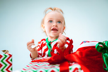 Image showing Cute baby girl 1 year old near santa hat posing over Christmas background. Sitting on floor with Christmas ball. Holiday season.