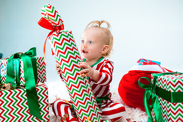 Image showing Cute baby girl 1 year old near santa hat posing over Christmas background. Sitting on floor with Christmas ball. Holiday season.