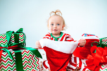 Image showing Cute baby girl 1 year old wearing santa hat posing over Christmas background. Sitting on floor with Christmas ball. Holiday season.