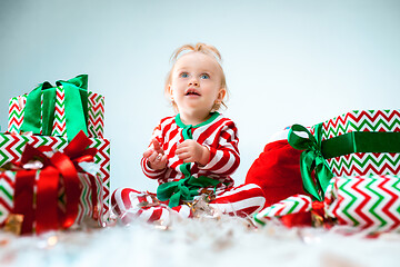 Image showing Cute baby girl 1 year old near santa hat posing over Christmas background. Sitting on floor with Christmas ball. Holiday season.