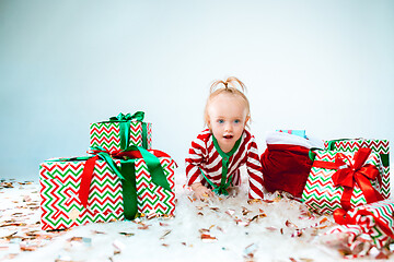 Image showing Cute baby girl 1 year old near santa hat posing over Christmas background. Sitting on floor with Christmas ball. Holiday season.