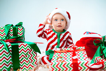 Image showing Cute baby girl 1 year old wearing santa hat posing over Christmas background. Sitting on floor with Christmas ball. Holiday season.