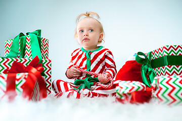 Image showing Cute baby girl 1 year old near santa hat posing over Christmas background. Sitting on floor with Christmas ball. Holiday season.