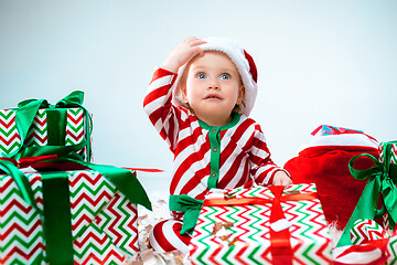 Image showing Cute baby girl 1 year old wearing santa hat posing over Christmas background. Sitting on floor with Christmas ball. Holiday season.