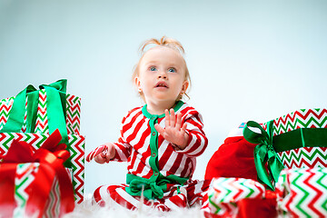 Image showing Cute baby girl 1 year old near santa hat posing over Christmas background. Sitting on floor with Christmas ball. Holiday season.