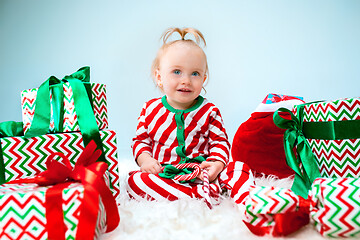 Image showing Cute baby girl 1 year old near santa hat posing over Christmas background. Sitting on floor with Christmas ball. Holiday season.