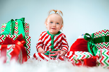 Image showing Cute baby girl 1 year old near santa hat posing over Christmas background. Sitting on floor with Christmas ball. Holiday season.