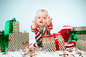 Image showing Cute baby girl 1 year old near santa hat posing over Christmas background. Sitting on floor with Christmas ball. Holiday season.