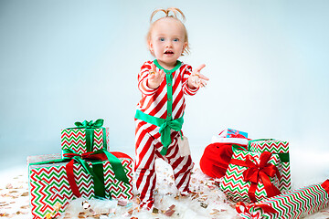 Image showing Cute baby girl 1 year old wearing santa hat posing over Christmas background. Sitting on floor with Christmas ball. Holiday season.