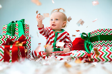 Image showing Cute baby girl 1 year old near santa hat posing over Christmas background. Sitting on floor with Christmas ball. Holiday season.