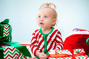 Image showing Cute baby girl 1 year old near santa hat posing over Christmas background. Sitting on floor with Christmas ball. Holiday season.