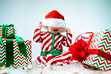 Image showing Cute baby girl 1 year old wearing santa hat posing over Christmas background. Sitting on floor with Christmas ball. Holiday season.