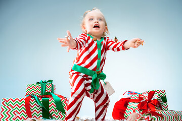 Image showing Cute baby girl 1 year old wearing santa hat posing over Christmas background. Sitting on floor with Christmas ball. Holiday season.