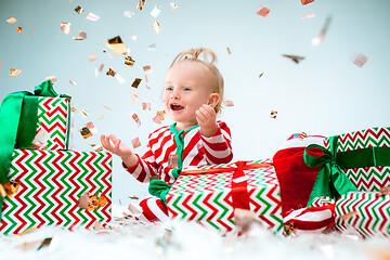 Image showing Cute baby girl 1 year old near santa hat posing over Christmas background. Sitting on floor with Christmas ball. Holiday season.