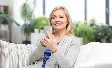 Image showing smiling woman with smartphone texting at home