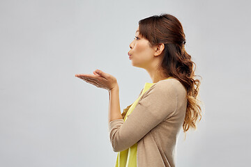 Image showing asian woman holding something on hand and blowing