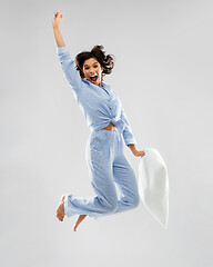 Image showing happy woman in blue pajama jumping with pillow