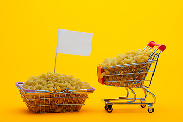 Image showing The cart and the basket are filled with pasta on a bright orange background, a flag is stuck in the basket