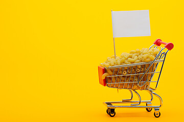 Image showing The grocery cart is filled with pasta on a bright orange background, a flag is stuck in the basket