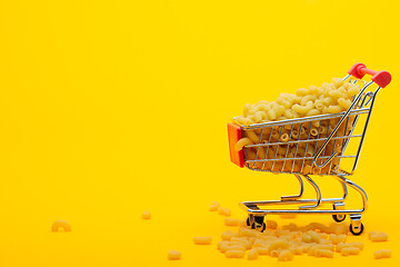 Image showing A grocery cart to the top is filled with pasta on a bright orange background, some pasta is lying next to the cart