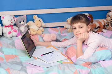 Image showing Schoolgirl does homework while lying in bed with a tablet