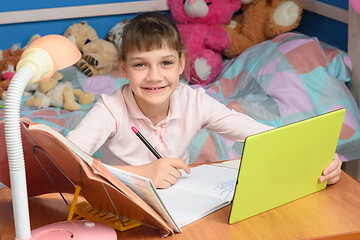 Image showing Cheerful girl doing homework using tablet computer