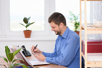 Image showing Successful office worker with a smile makes an entry in a notebook