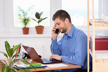 Image showing Young businessman talking on the phone in the office and working in a laptop