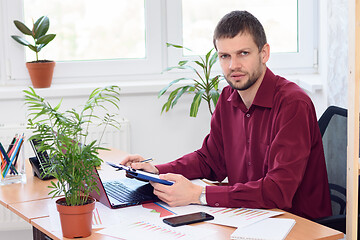 Image showing Pensive office specialist sits at a table in the office and looked into the frame