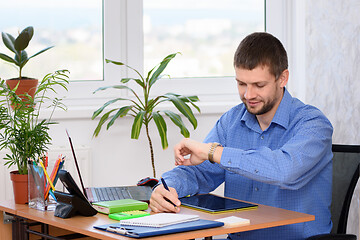 Image showing A businessman looks at a watch while in the office at his workplace