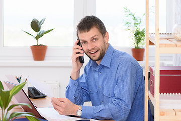 Image showing Businessman talking on the phone at his workplace and looking in the frame.