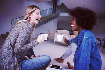 Image showing young multiethnic women sit on the floor and drinking coffee