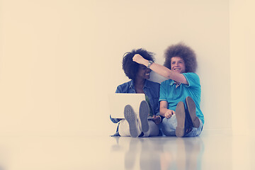 Image showing multiethnic couple sitting on the floor with a laptop and tablet